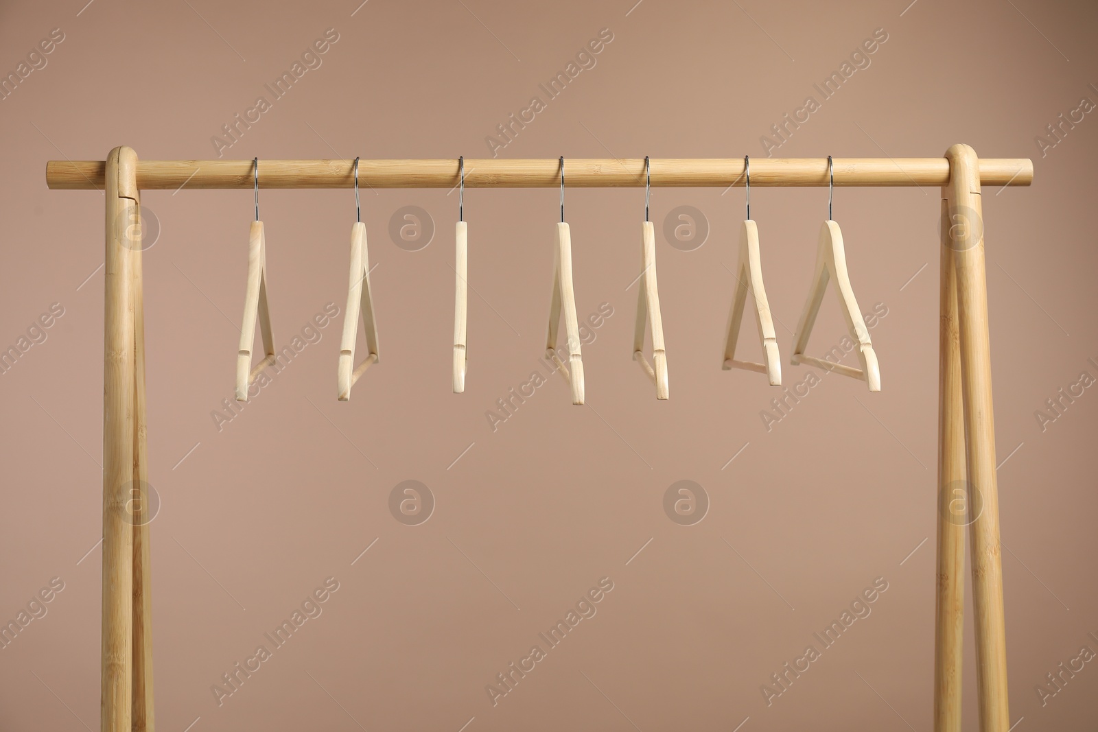 Photo of Empty clothes hangers on wooden rack against light brown background