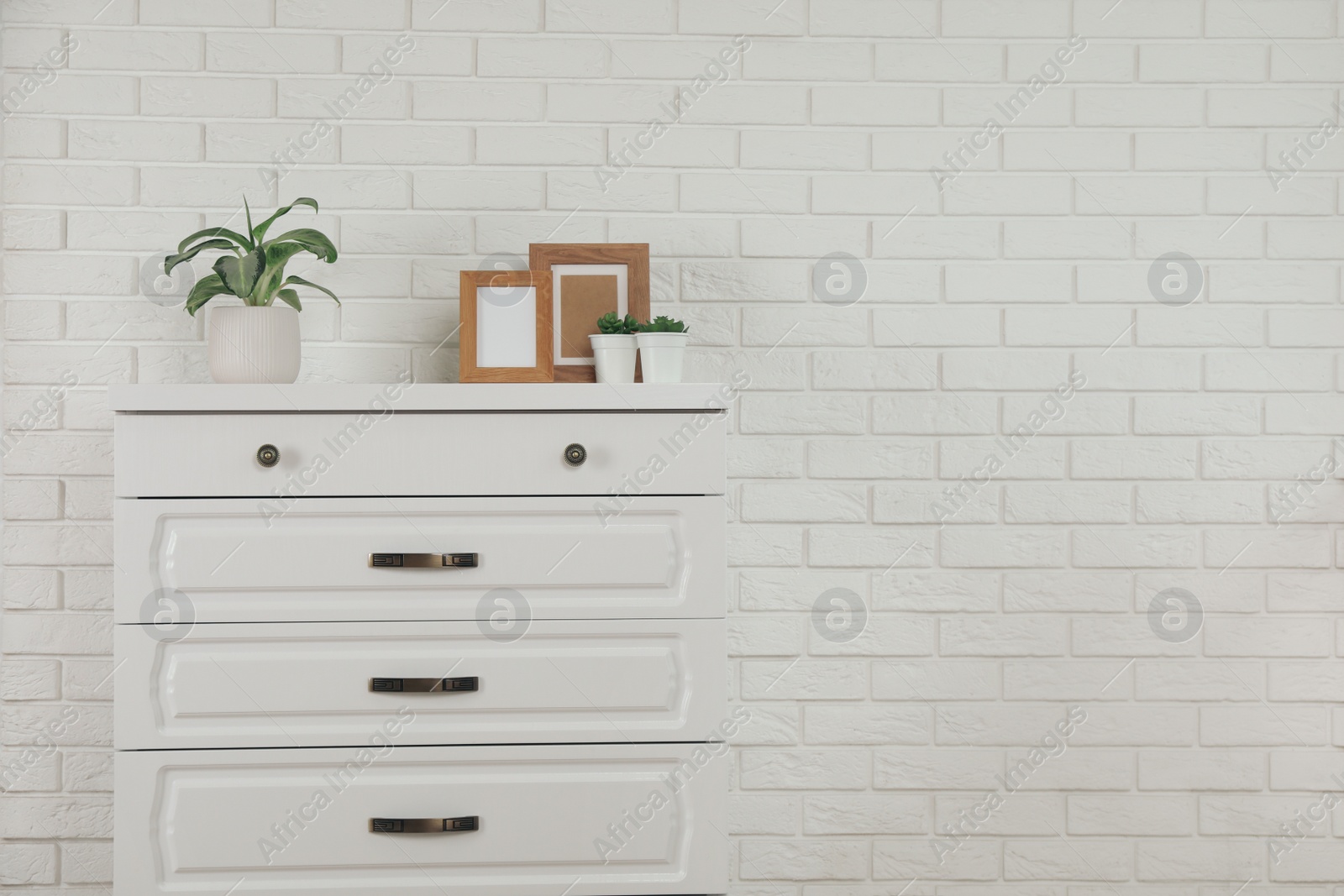 Photo of Modern chest of drawers with decor near white brick wall. Space for text