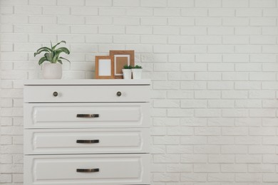 Modern chest of drawers with decor near white brick wall. Space for text