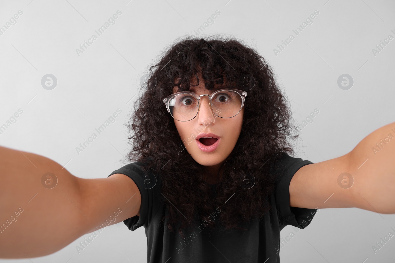 Photo of Beautiful young woman in eyeglasses taking selfie on light grey background