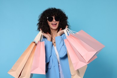 Photo of Happy young woman with shopping bags and stylish sunglasses on light blue background