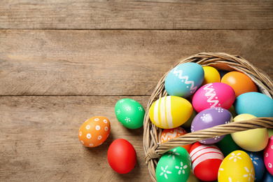 Colorful Easter eggs in basket on wooden background, flat lay. Space for text