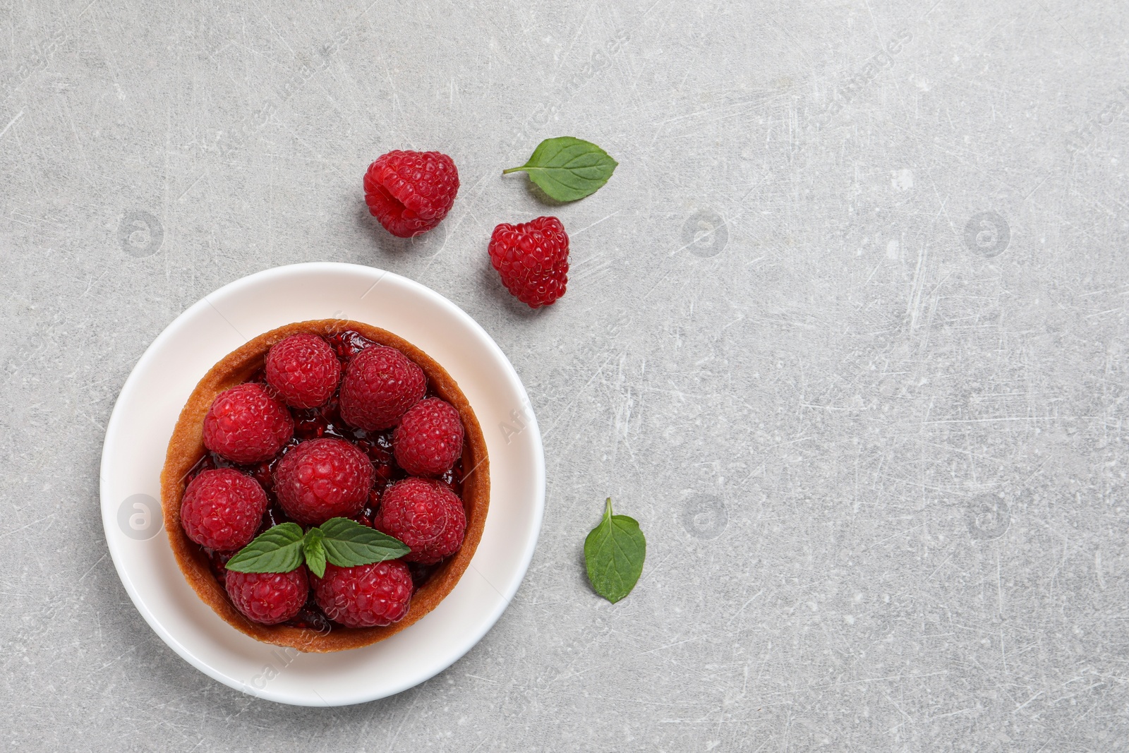 Photo of Tartlet with fresh raspberries and mint on light grey table, top view with space for text. Delicious dessert