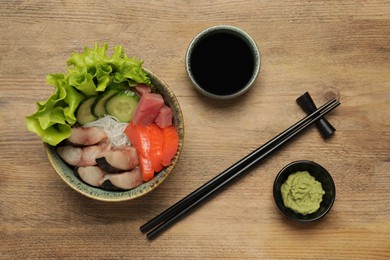 Photo of Delicious mackerel, salmon and tuna served with funchosa, cucumbers, lettuce, wasabi and soy sauce on wooden table, flat lay. Tasty sashimi dish