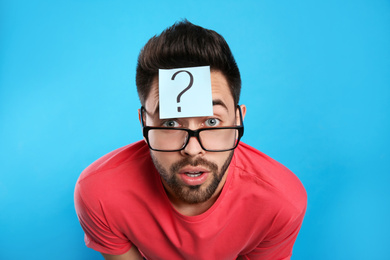 Emotional young man with question mark sticker on forehead against light blue background