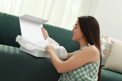 Happy young woman opening parcel at home. Internet shopping