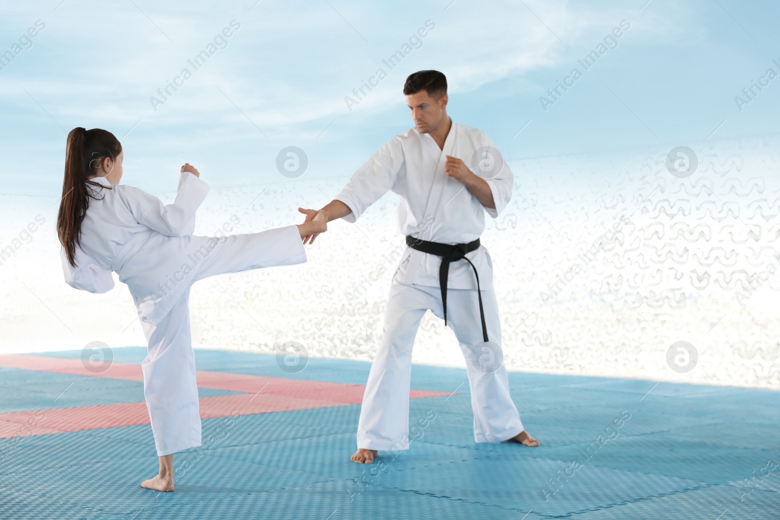 Photo of Girl practicing karate with coach on tatami outdoors