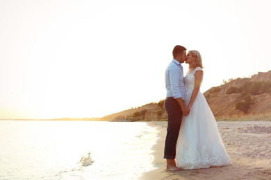 Photo of Wedding couple holding hands and kissing on beach. Space for text