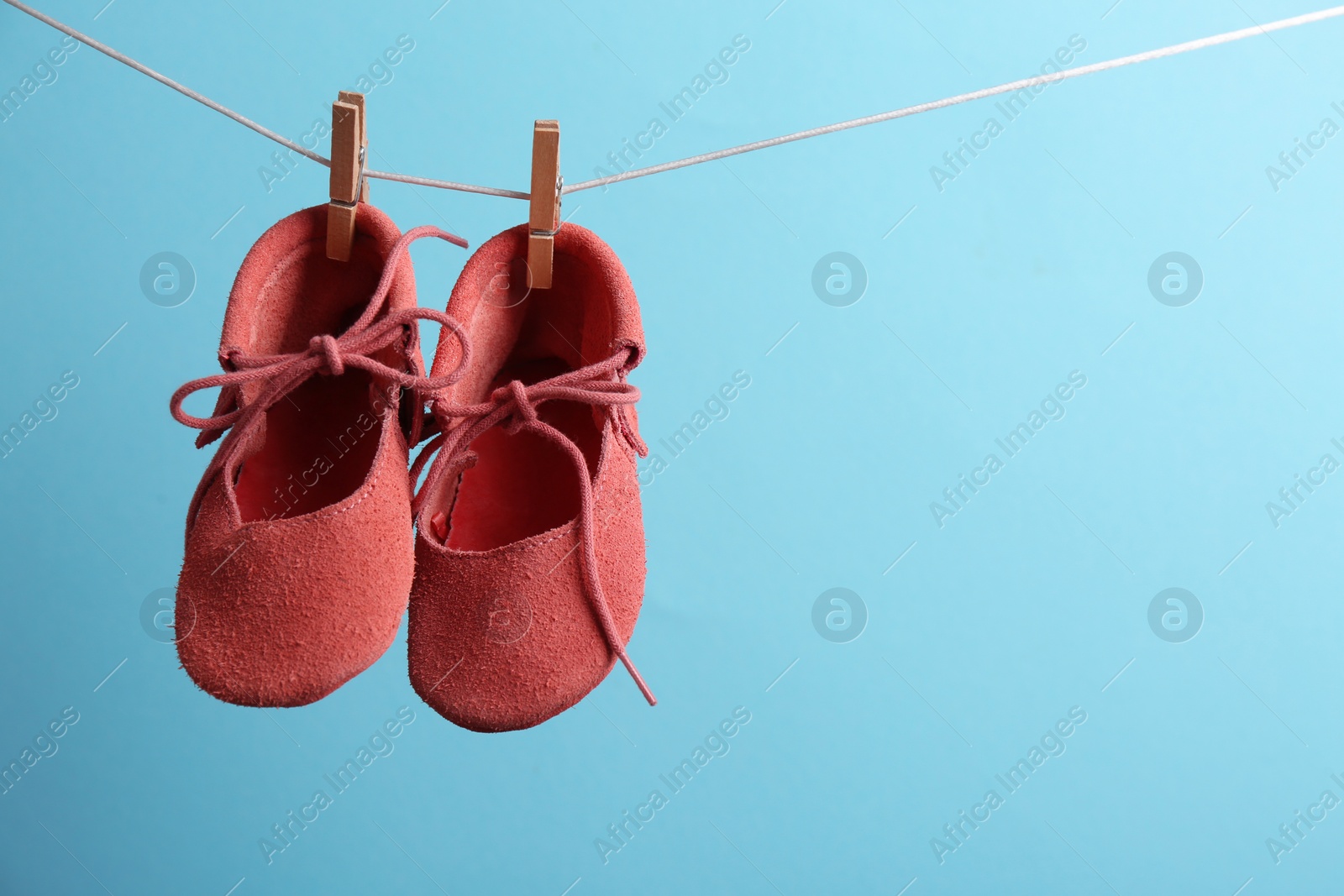 Photo of Cute small shoes hanging on washing line against color background, space for text. Baby accessories