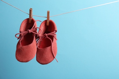 Photo of Cute small shoes hanging on washing line against color background, space for text. Baby accessories