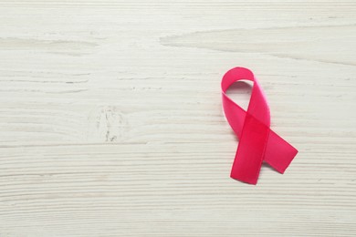 Photo of Breast cancer awareness. Pink ribbon on white wooden table, top view. Space for text