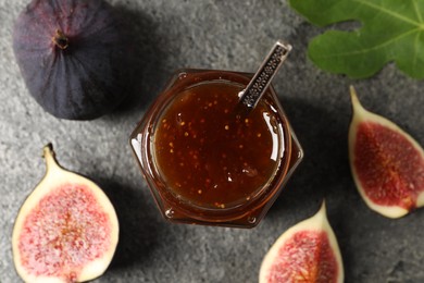 Photo of Glass jar with tasty sweet jam, fresh figs and green leaf on grey textured table, flat lay