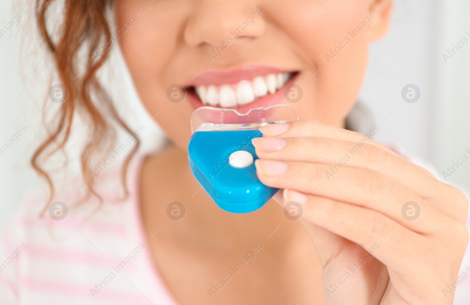 Photo of Young African-American woman using teeth whitening device on light background, closeup