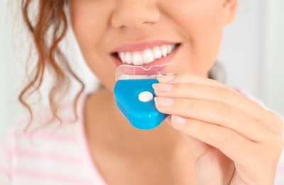 Photo of Young African-American woman using teeth whitening device on light background, closeup