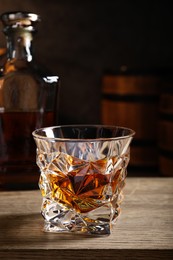 Photo of Glass with whiskey on table against wooden barrels