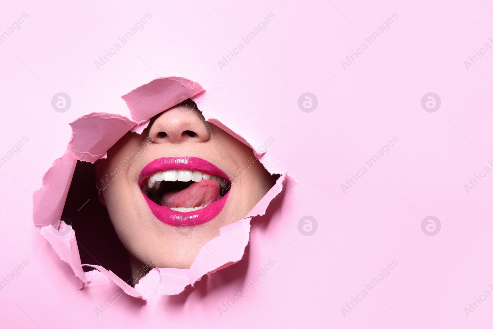 Photo of View of beautiful young woman with perfect lips makeup through hole in color paper. Space for text