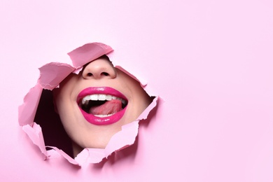 Photo of View of beautiful young woman with perfect lips makeup through hole in color paper. Space for text