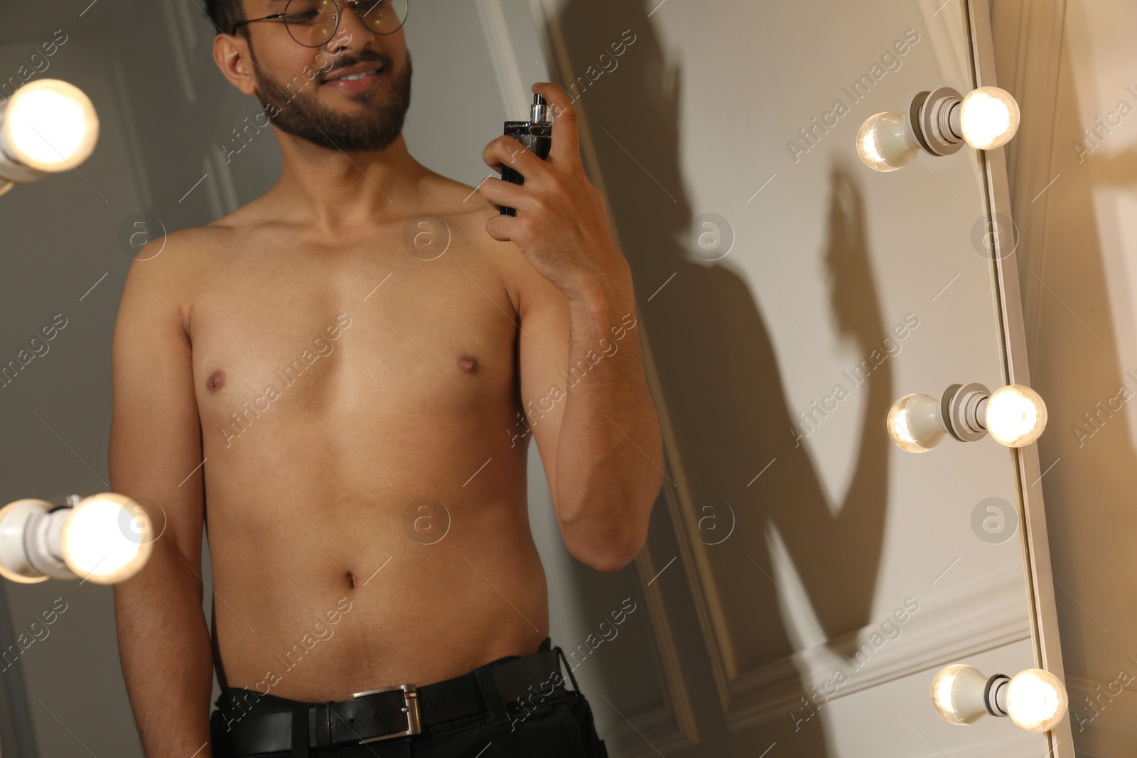 Photo of Man spraying luxury perfume near mirror indoors, closeup