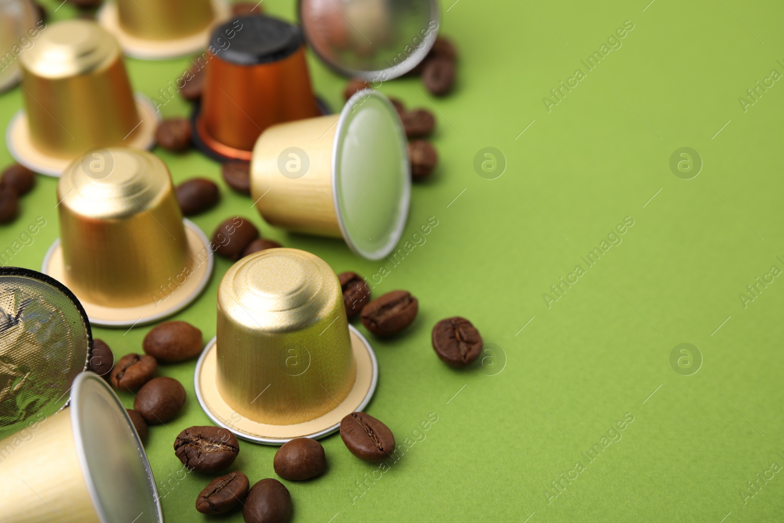 Photo of Many coffee capsules and beans on green background, closeup. Space for text