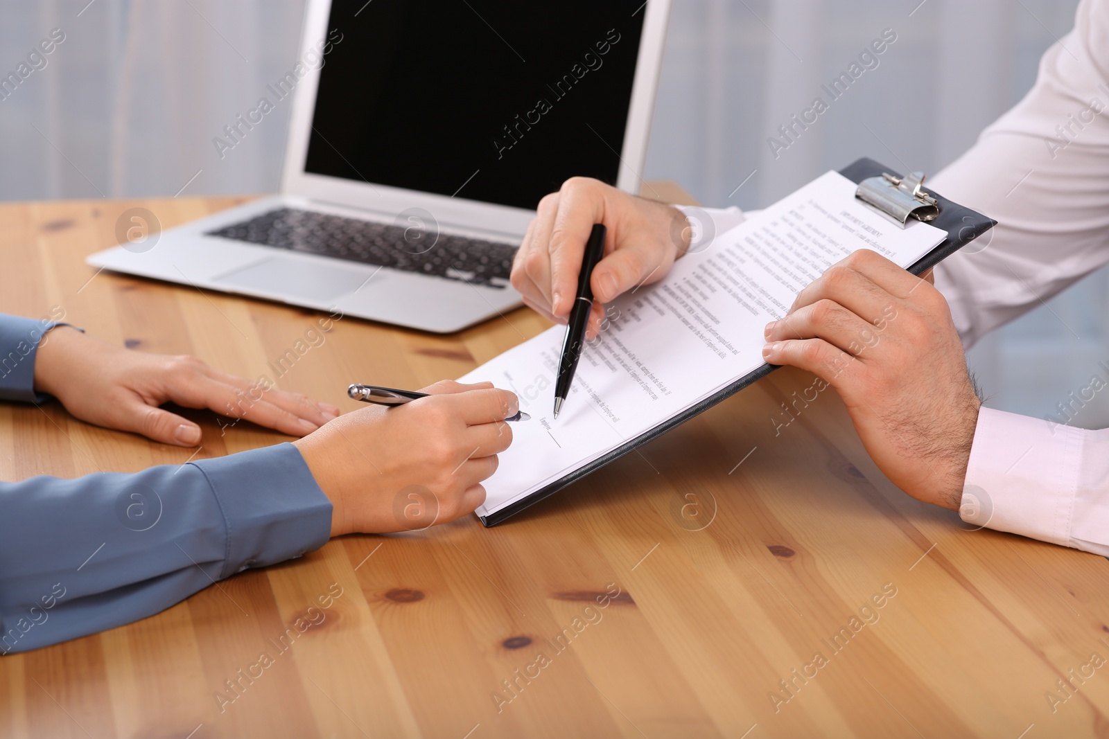 Photo of Businesspeople signing contract at wooden table in office, closeup of hands