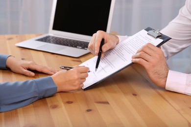 Businesspeople signing contract at wooden table in office, closeup of hands