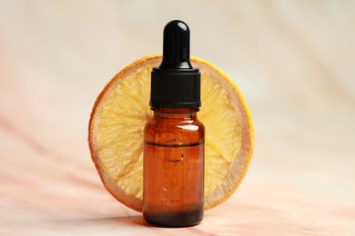 Bottle of organic cosmetic product and dried orange slice on pink marbled background, closeup