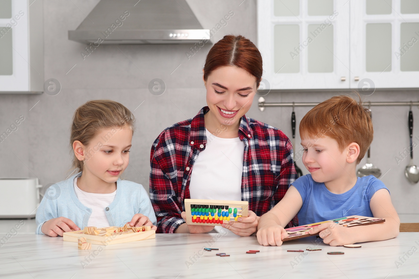 Photo of Happy mother and children playing with different math game kits at white marble table in kitchen. Study mathematics with pleasure