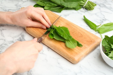 Photo of Woman cutting sorrel leaves at white marble table, closeup