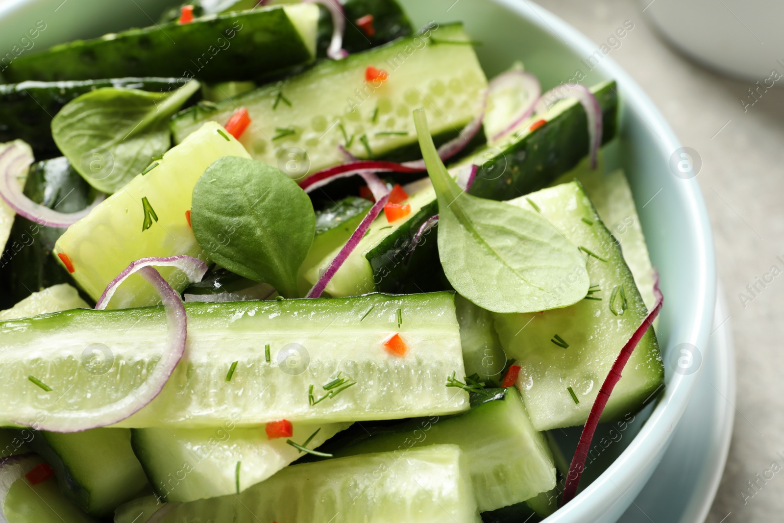 Photo of Delicious cucumber salad with onion and spinach in bowl, closeup