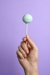 Woman holding sweet cake pop on lilac background, closeup