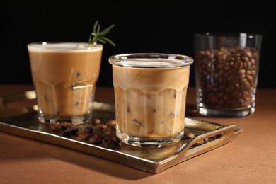 Photo of Refreshing iced coffee with milk in glasses and beans on brown table