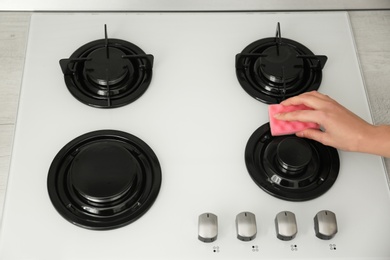 Photo of Woman cleaning gas stove with sponge, closeup