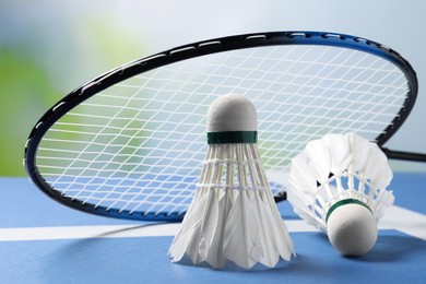 Feather badminton shuttlecocks and racket on blue table against blurred background, closeup