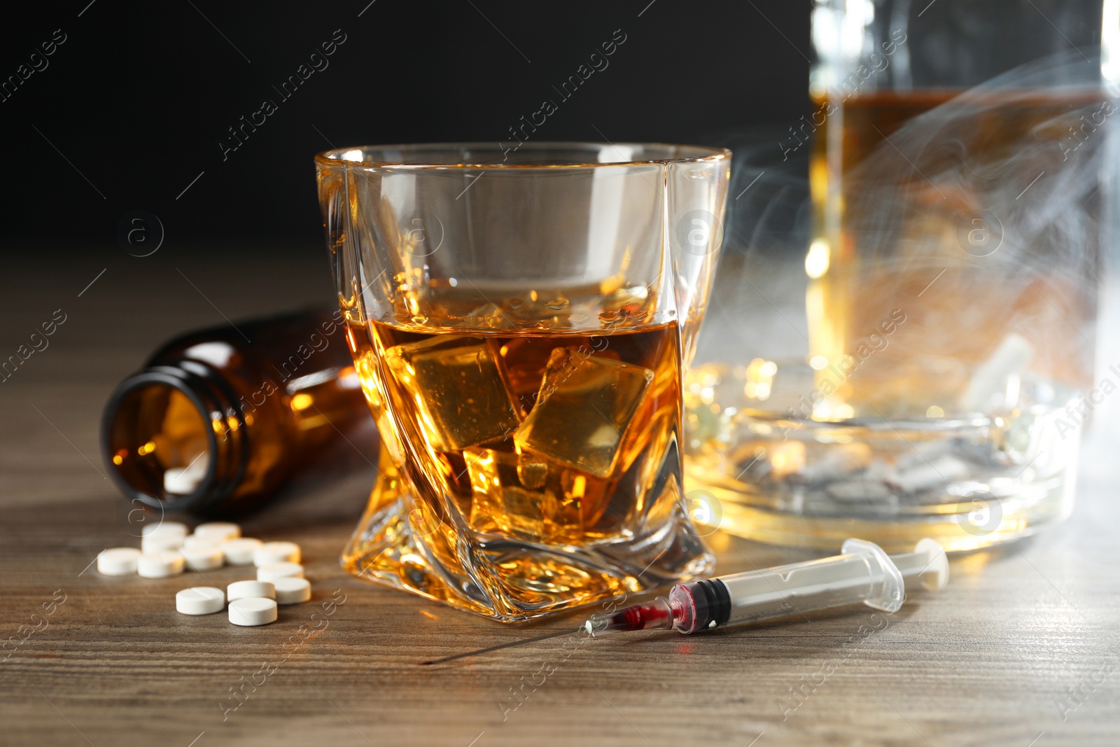 Photo of Alcohol and drug addiction. Whiskey in glass, syringe, pills and cigarettes on wooden table