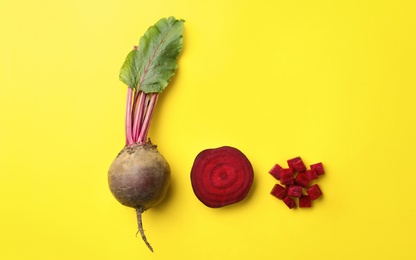 Photo of Whole and cut fresh red beets on yellow background, flat lay