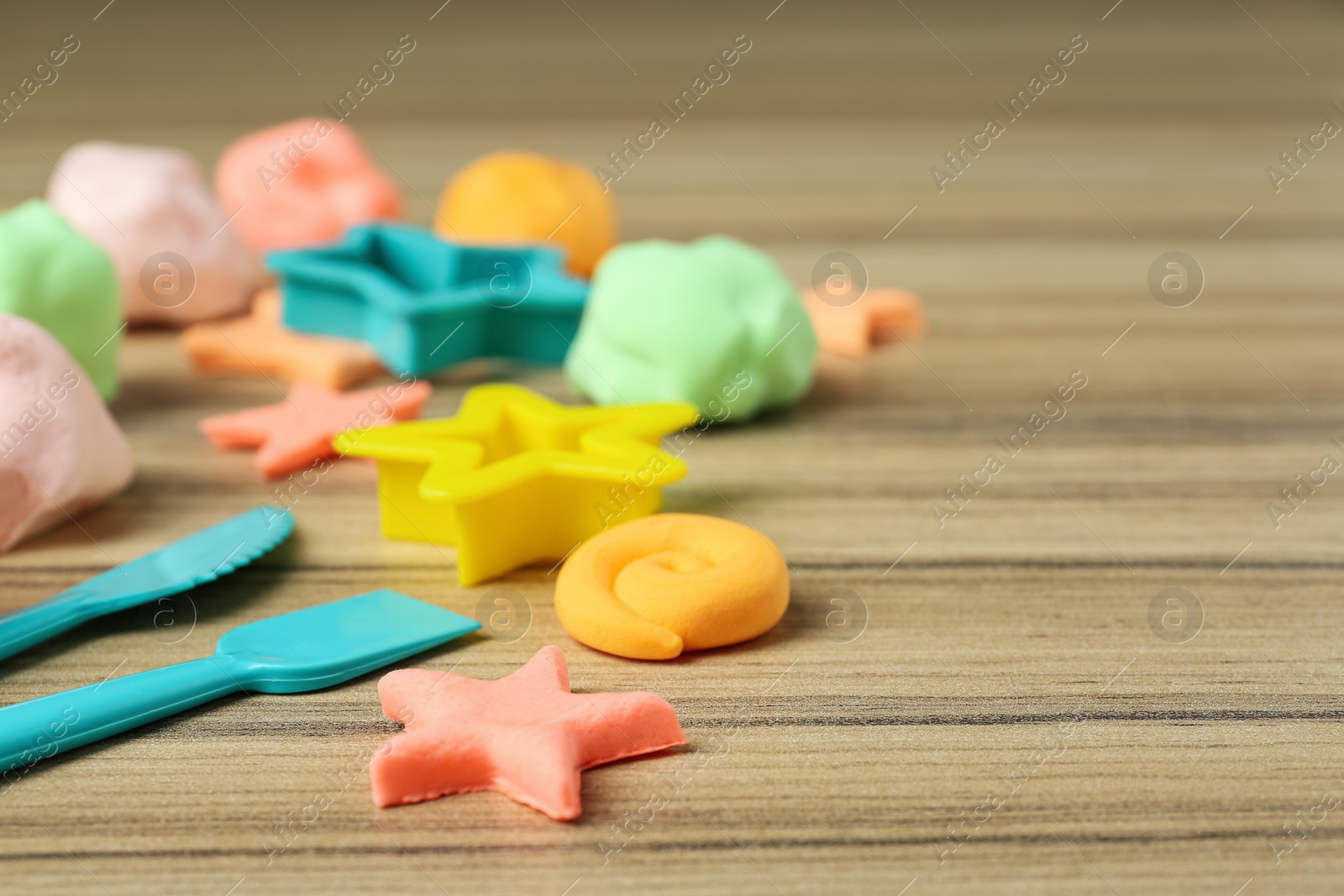 Photo of Different color play dough with tools and molds on wooden table, closeup. Space for text