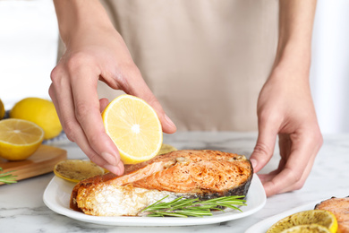 Photo of Woman adding lemon juice to cooked red fish on white marble table, closeup