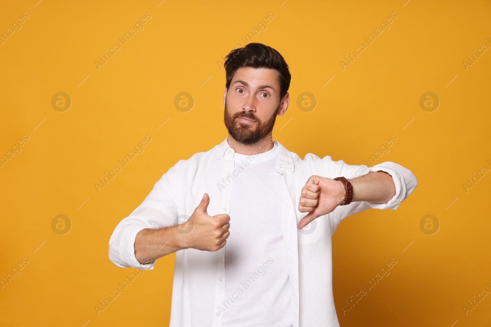 Photo of Handsome bearded man showing thumbs up and down on orange background