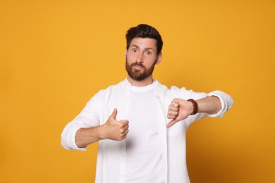 Handsome bearded man showing thumbs up and down on orange background