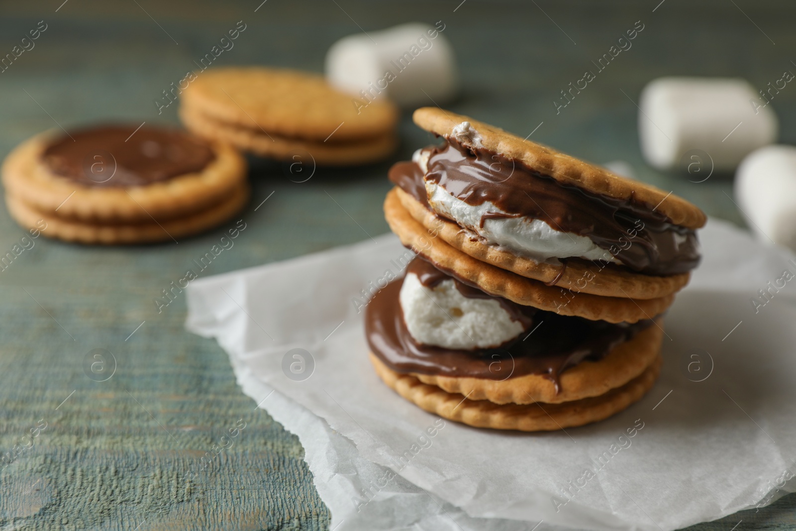 Photo of Delicious marshmallow sandwiches with crackers and chocolate on light blue wooden table, closeup. Space for text