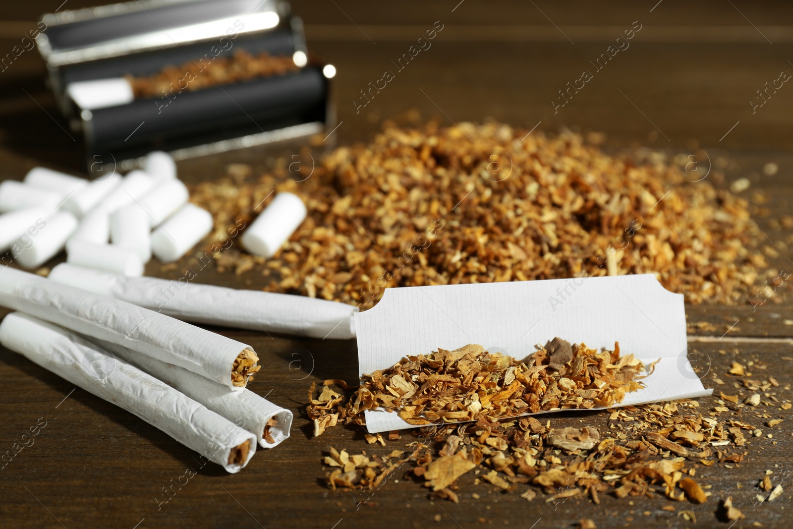 Photo of Tobacco, hand rolled cigarettes and roller on wooden table, closeup