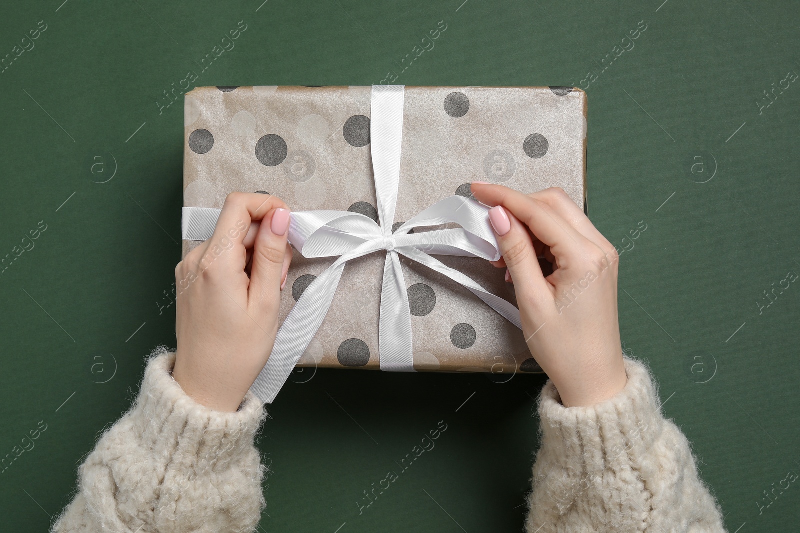 Photo of Christmas present. Woman holding gift box on dark green background, top view