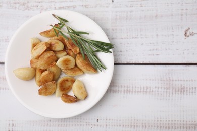 Photo of Fried garlic cloves and rosemary on wooden table, top view. Space for text