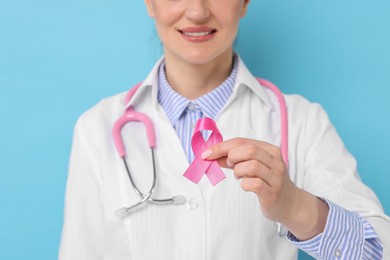 Mammologist with pink ribbon against light blue background, closeup. Breast cancer awareness