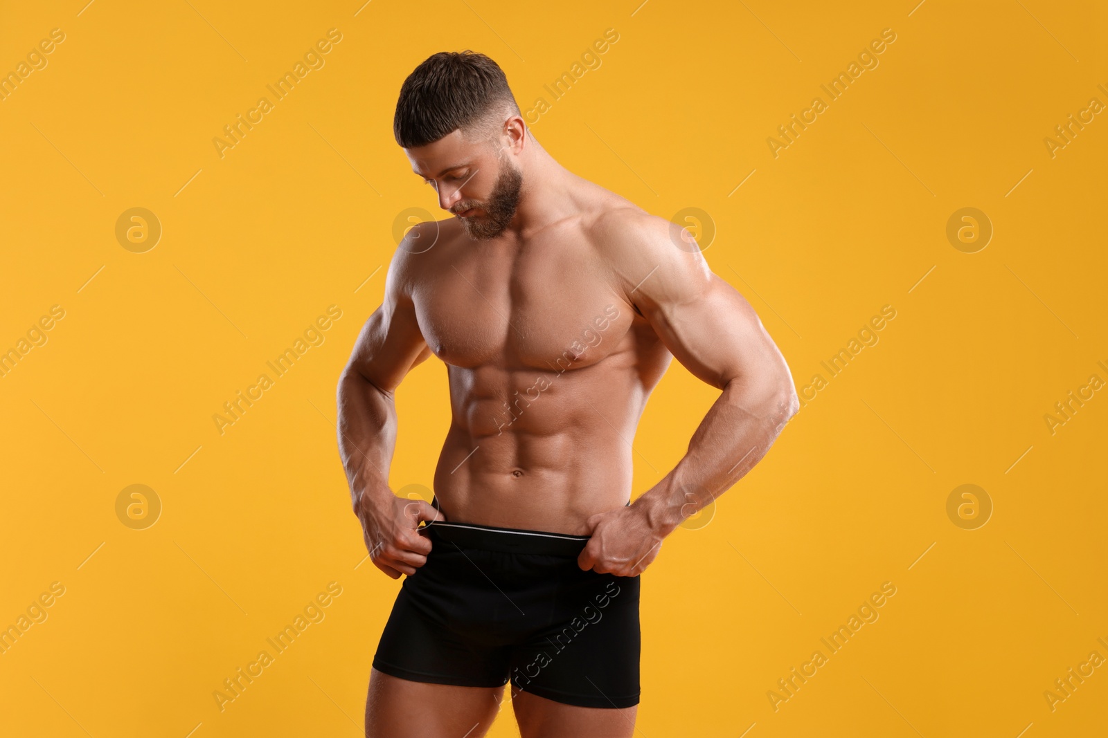 Photo of Young man is stylish black underwear on orange background