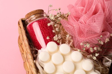 Photo of Spa gift set of different luxury products in wicker basket on pale pink background, closeup