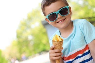 Cute little boy with delicious ice cream outdoors, space for text