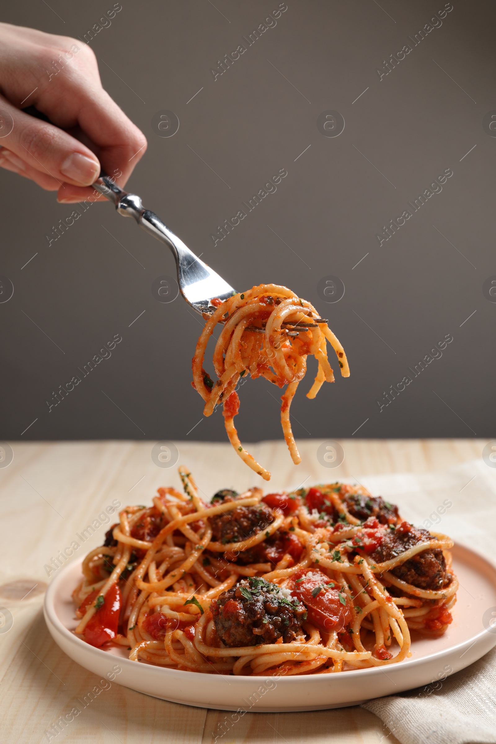 Photo of Woman eating delicious pasta with meatballs at wooden table, closeup
