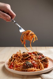 Woman eating delicious pasta with meatballs at wooden table, closeup