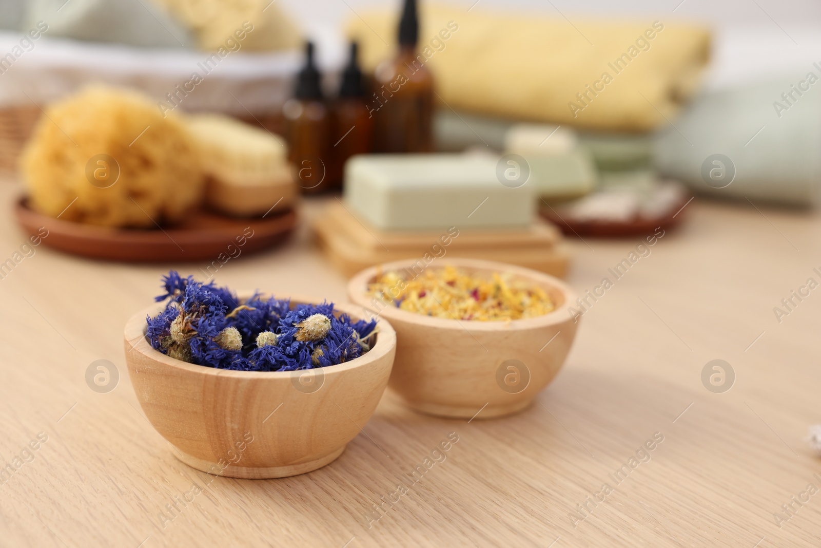 Photo of Bowls with dry flowers on light wooden table, space for text. Spa therapy